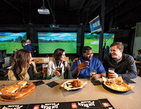 A group of four people sitting at a bar in X Golf, eating and drinking