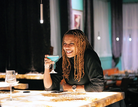 A woman sitting at the bar at Elle Restaurant and Lounge in Solon, Ohio, holding a blue drink and smiling